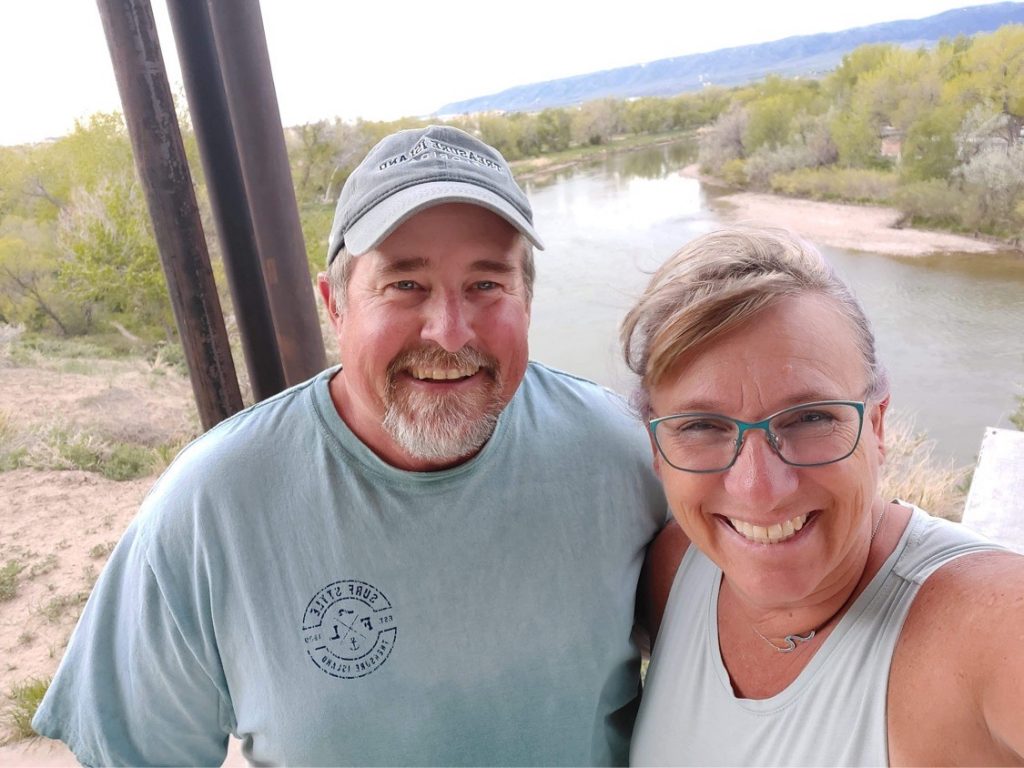 A man and a woman smiling in front of a river.